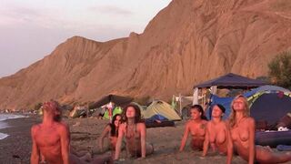 A group of naked people play volleyball on the sandy beach